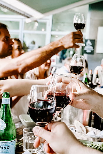 Celebrate with friends during a casual indoor gathering, raising glasses of red wine in a toast. HD phone wallpaper