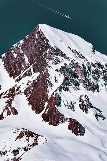 Epic aerial shot of a snowy mountain summit with an airplane flying overhead. HD phone wallpaper