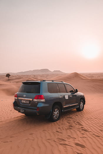 A rugged SUV traverses the sandy dunes of Dubai's desert at sunset, displaying adventure and exploration. HD phone wallpaper