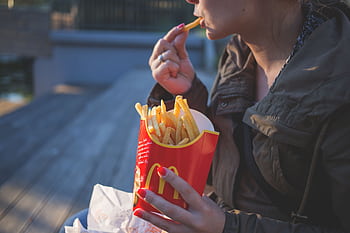 Close-up of a woman enjoying French fries outdoors with a casual vibe. HD wallpaper