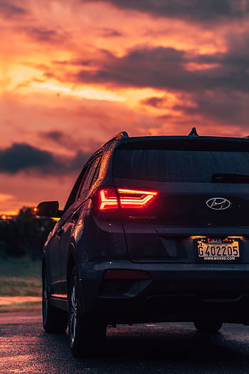 Rear view of a modern Hyundai SUV on a wet road during a vibrant sunset, showcasing dramatic cloudscape. HD phone wallpaper