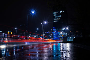 Illuminated city street at night with vibrant light trails and urban skyline. HD wallpaper
