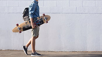 Casual young man walking with longboard against a white brick wall in Sanger, California. HD wallpaper