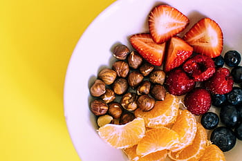 Close-up of a bowl with fresh fruits and nuts against a vibrant yellow backdrop. HD wallpaper