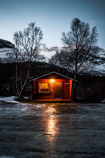 A cozy cabin illuminated amidst a snowy landscape in Skibotn, Norway at dawn. HD phone wallpaper