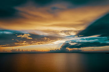Captivating sunset over tranquil ocean waters, framed by dramatic storm clouds and vibrant colors. HD wallpaper