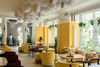 A stylish and spacious café with modern decor, yellow accents, and lush greenery. HD wallpaper