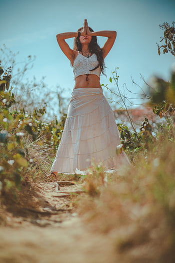 Young woman meditating in a peaceful outdoor setting wearing a white skirt. HD phone wallpaper