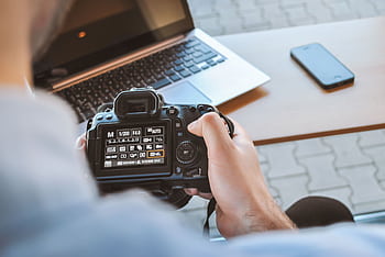 Close-up of hands holding DSLR camera at a workspace with laptop and smart. HD wallpaper