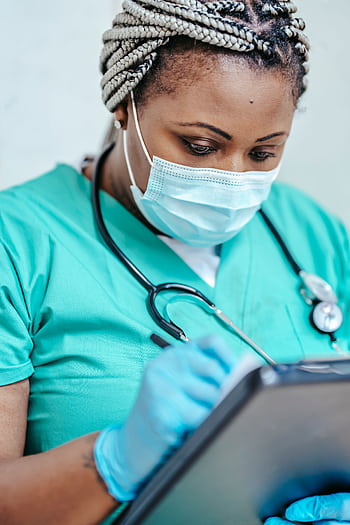 Nurse with mask and gloves reviewing documents on clipboard in a clinic setting. HD phone wallpaper