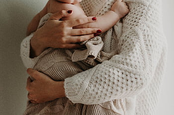 Close-up of a mother holding her baby in warm knitwear, conveying love and togetherness. HD wallpaper