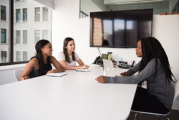 Three women collaborate in a modern office setting, discussing business plans and teamwork. HD wallpaper