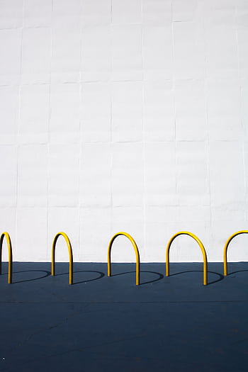 Modern minimalist of yellow bike racks casting shadows on a blue surface against a white wall. HD phone wallpaper