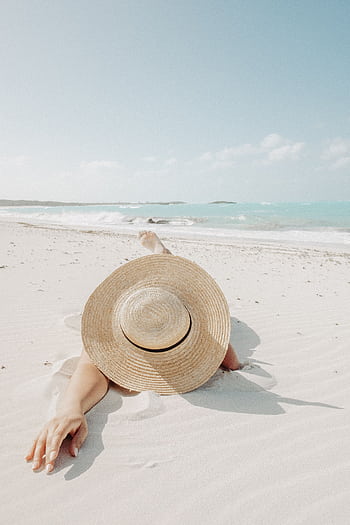 A woman in a straw hat relaxing on a serene tropical beach on a sunny day. HD phone wallpaper