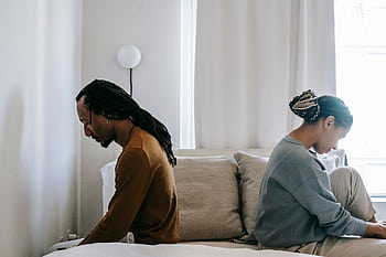 African American couple sitting back to back on a bed, depicting relationship conflict at home. HD wallpaper