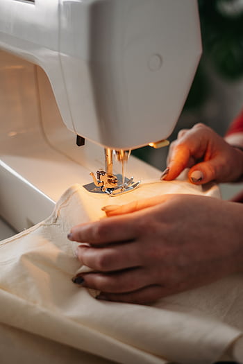 Detailed view of sewing process with hands guiding fabric on a machine. HD phone wallpaper