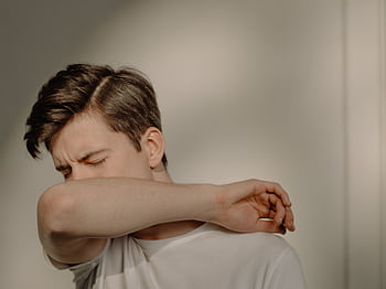 A young man sneezes into his elbow, showcasing a hygiene practice, in an indoor setting. HD wallpaper