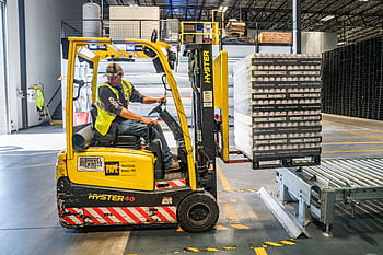 A warehouse worker maneuvers a forklift to transport crates for brewing company storage. HD wallpaper