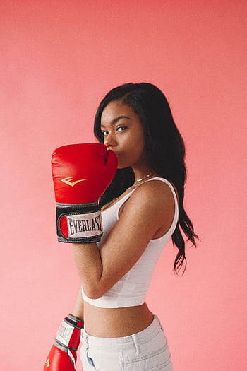 Stylish woman posing with red boxing gloves on a pink background, exuding confidence and fitness. HD phone wallpaper