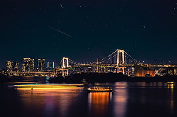 Night view of Tokyo's Rainbow Bridge under a starry sky, reflecting city lights on the water. HD wallpaper