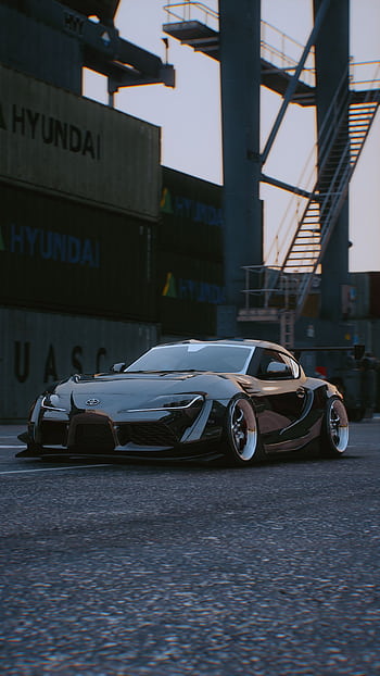 A luxury black sports car parked at an industrial dock with shipping containers and cranes. HD phone wallpaper