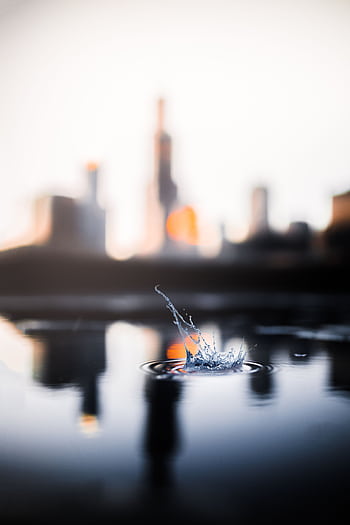 A captivating view of a water splash with a blurred city skyline in the background. HD phone wallpaper