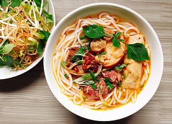 A colorful bowl of Vietnamese noodle soup with fresh herbs and vegetables. HD wallpaper