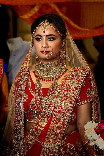 Beautiful Indian bride in a red and gold lehenga with intricate jewelry, posing elegantly indoors. HD phone wallpaper