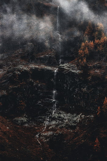 A serene waterfall cascades down rocky cliffs, enveloped in mist, creating a tranquil nature scene. HD phone wallpaper