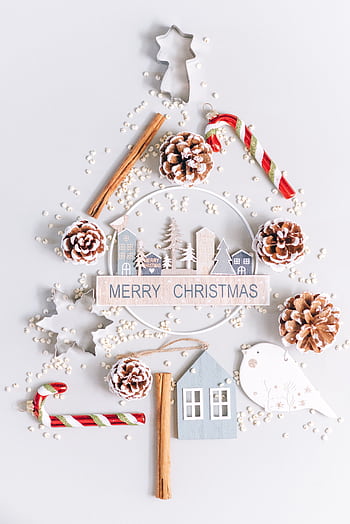 Festive flatlay of Christmas tree with ornaments, candy canes, and pinecones on white background. HD phone wallpaper