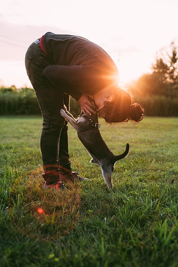 A woman bends down to kiss her playful puppy in a sunny outdoor field. HD phone wallpaper