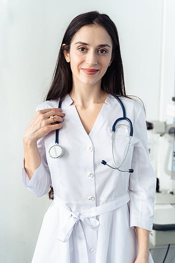 Portrait of a smiling female healthcare worker in a white coat with a stethoscope, embodying professionalism and care. HD phone wallpaper