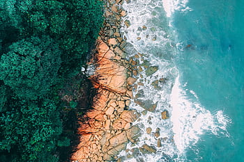 Stunning aerial view of a tropical coastline with lush greenery and crashing ocean waves. HD wallpaper