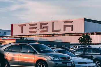 Tesla factory with parked cars during sunset, showcasing modern automotive industry vibes. HD wallpaper