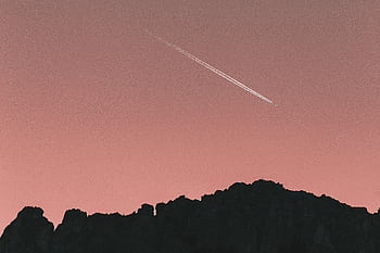 A scenic silhouette of mountains with a jet airplane streaking across the pink twilight sky. HD wallpaper