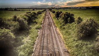 Aerial view of railway tracks through green countryside at sunset, illustrating travel and nature. HD wallpaper