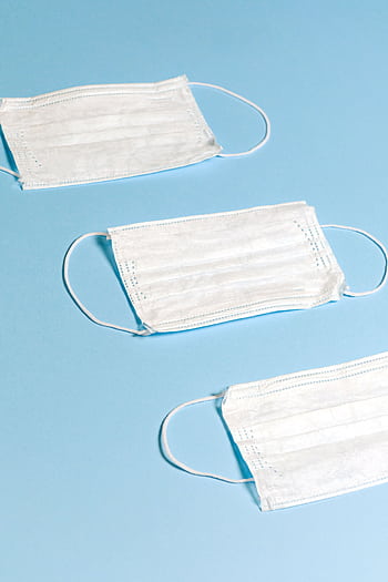 Three white face masks arranged on a pastel blue background, symbolizing health protection. HD phone wallpaper