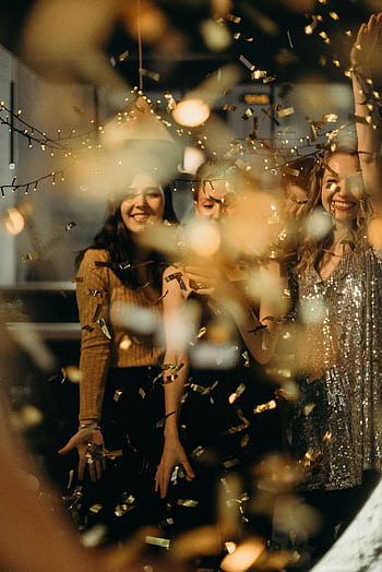 Women celebrating with confetti and string lights, capturing festive joy and excitement. HD phone wallpaper