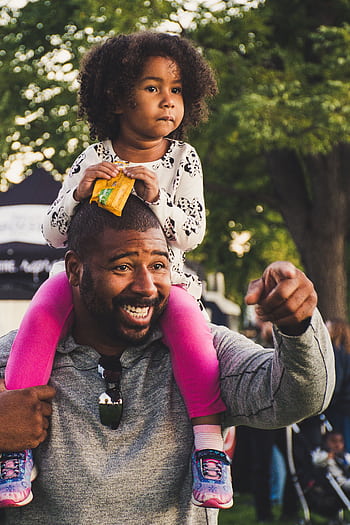 A joyful African American father with curly-haired daughter on shoulders, outdoors. HD phone wallpaper