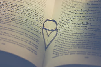 A ring casts a heart-shaped shadow on the pages of an open book, symbolizing love and romance. HD wallpaper