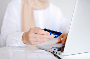 Close-up of a person holding a credit card while using a laptop for online shopping. HD wallpaper