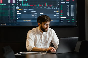 Professional analyzing stock market trends using laptop and digital display in modern office. HD wallpaper