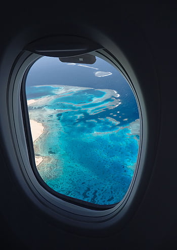 Breathtaking aerial view of ocean reefs through an airplane window, showcasing vibrant blues from above. HD phone wallpaper