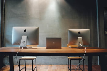 Minimalist office space with dual monitors on a wooden table, promoting a contemporary work environment. HD wallpaper