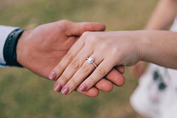 Romantic gesture of couple holding hands, showcasing a diamond engagement ring. HD wallpaper