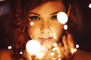 Enchanting close-up of a woman with red hair and freckles surrounded by glowing fairy lights. HD wallpaper