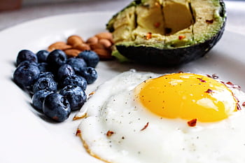 A nutritious breakfast featuring a fried egg, avocado, blueberries, and almonds. HD wallpaper