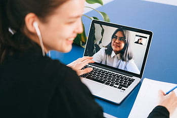 Woman having a video conference on a laptop, smiling and taking notes. HD wallpaper