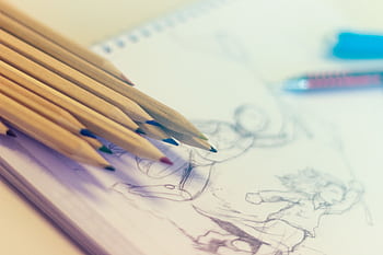 Close-up of colored pencils on sketch-filled notepad, perfect for creativity concepts. HD wallpaper