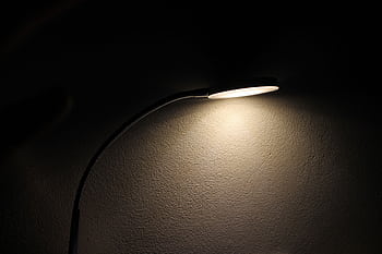 A sleek desk lamp casts a soft glow on a textured wall, creating a moody ambiance. HD wallpaper